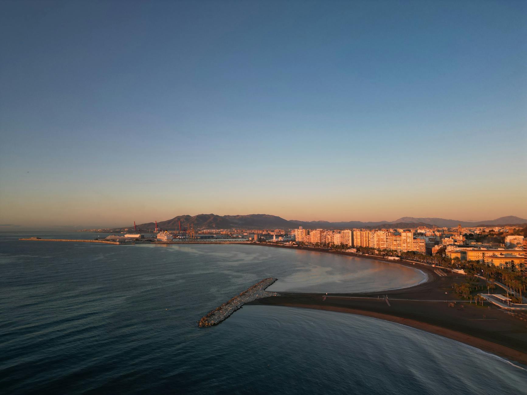 Aerial view of Málaga's coastline with sunlit buildings at sunset, showcasing the beautiful bay.