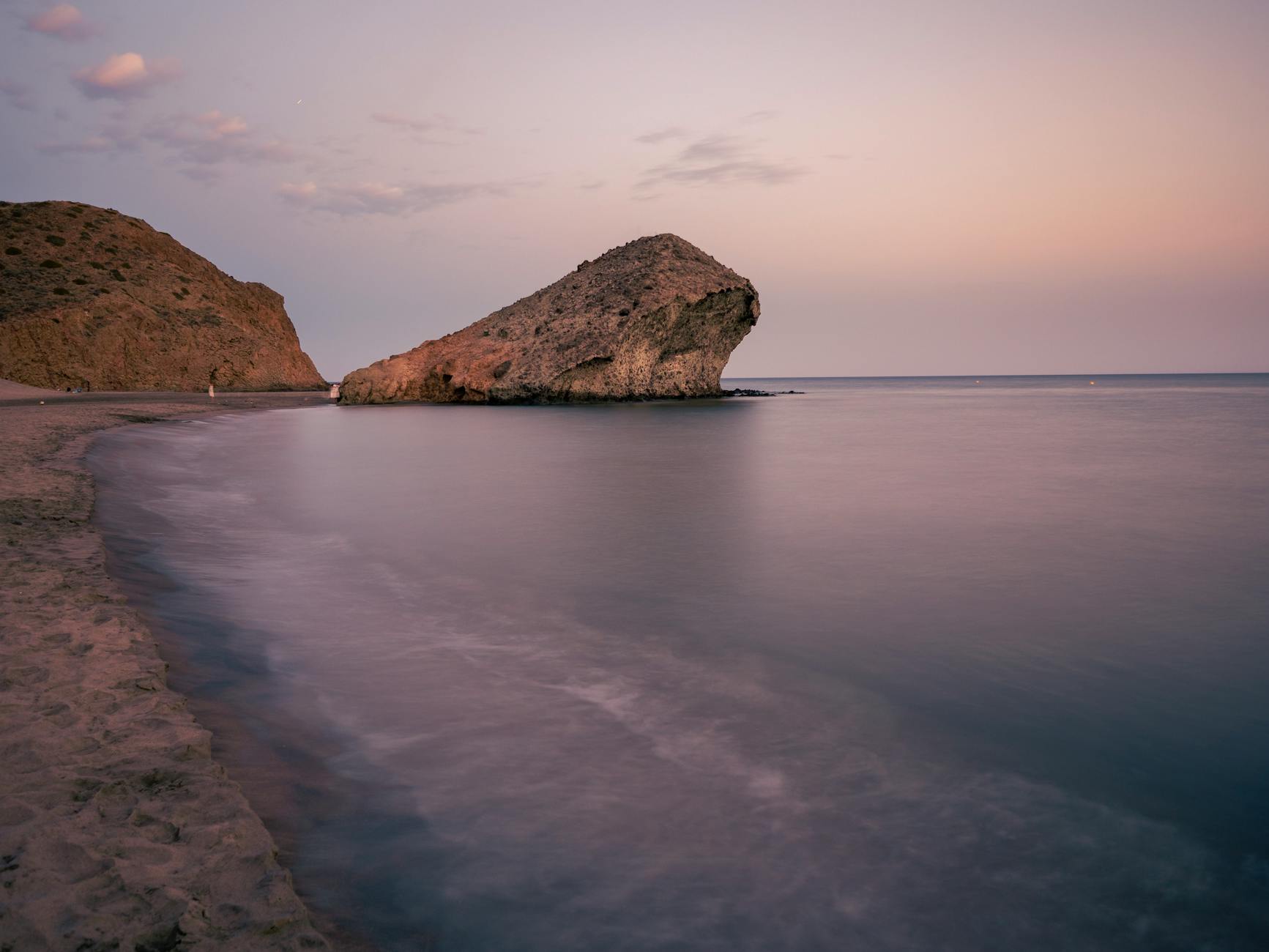 Serene view of a coastal rock formation at dusk in Almería, Spain, with calm seas and a pastel sky.