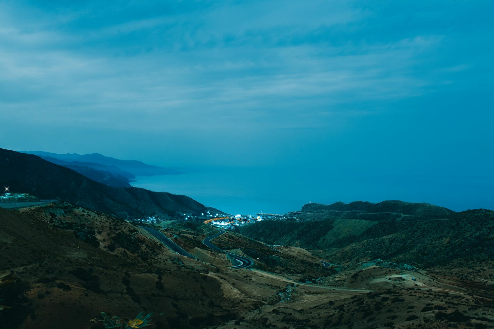 A breathtaking coastal landscape of El Jebha, Morocco, at dusk featuring winding roads and serene ocean views.