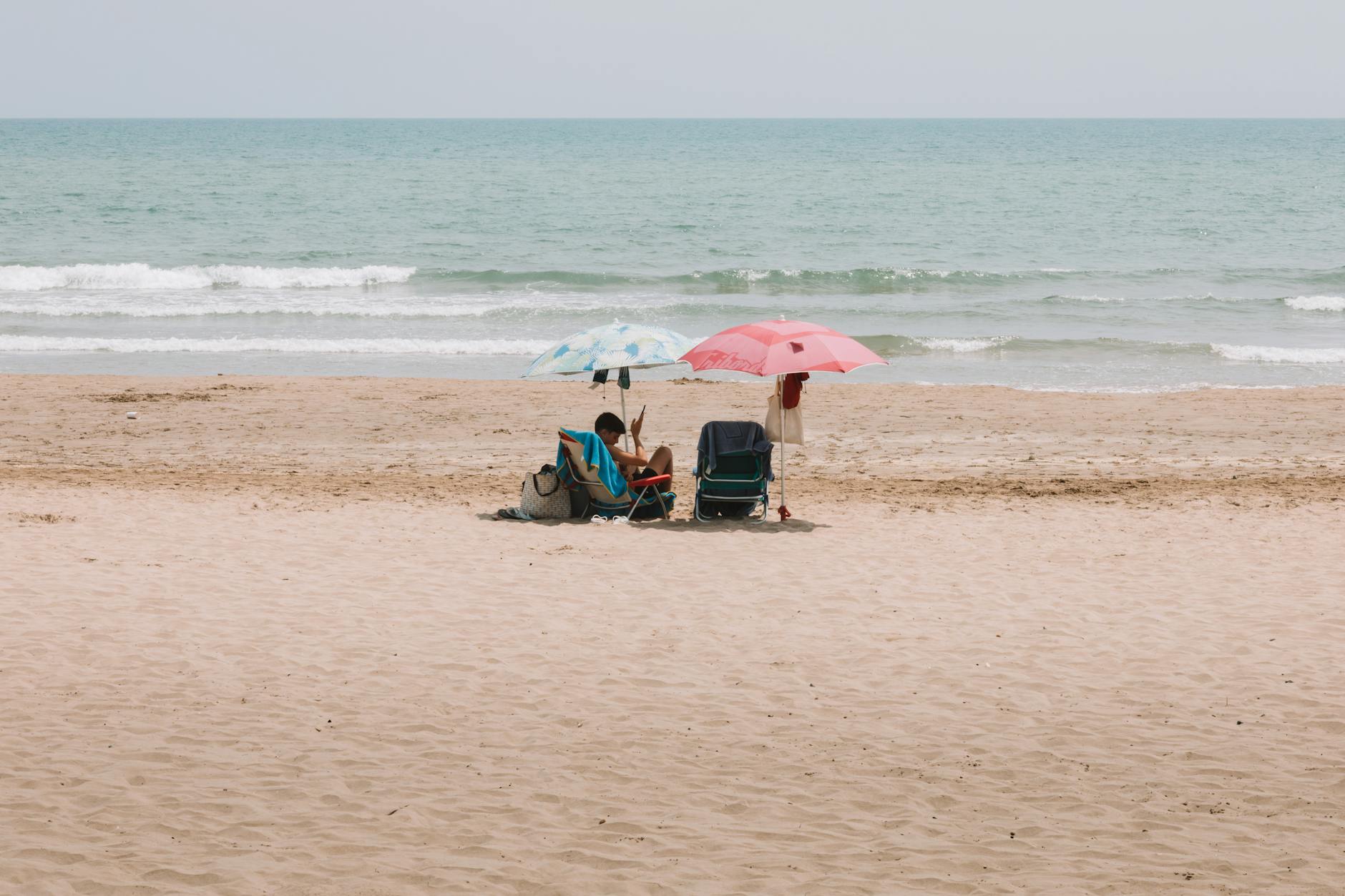 A peaceful day at the sandy beach in Benidorm, Spain with umbrellas and sunbeds by the shore.