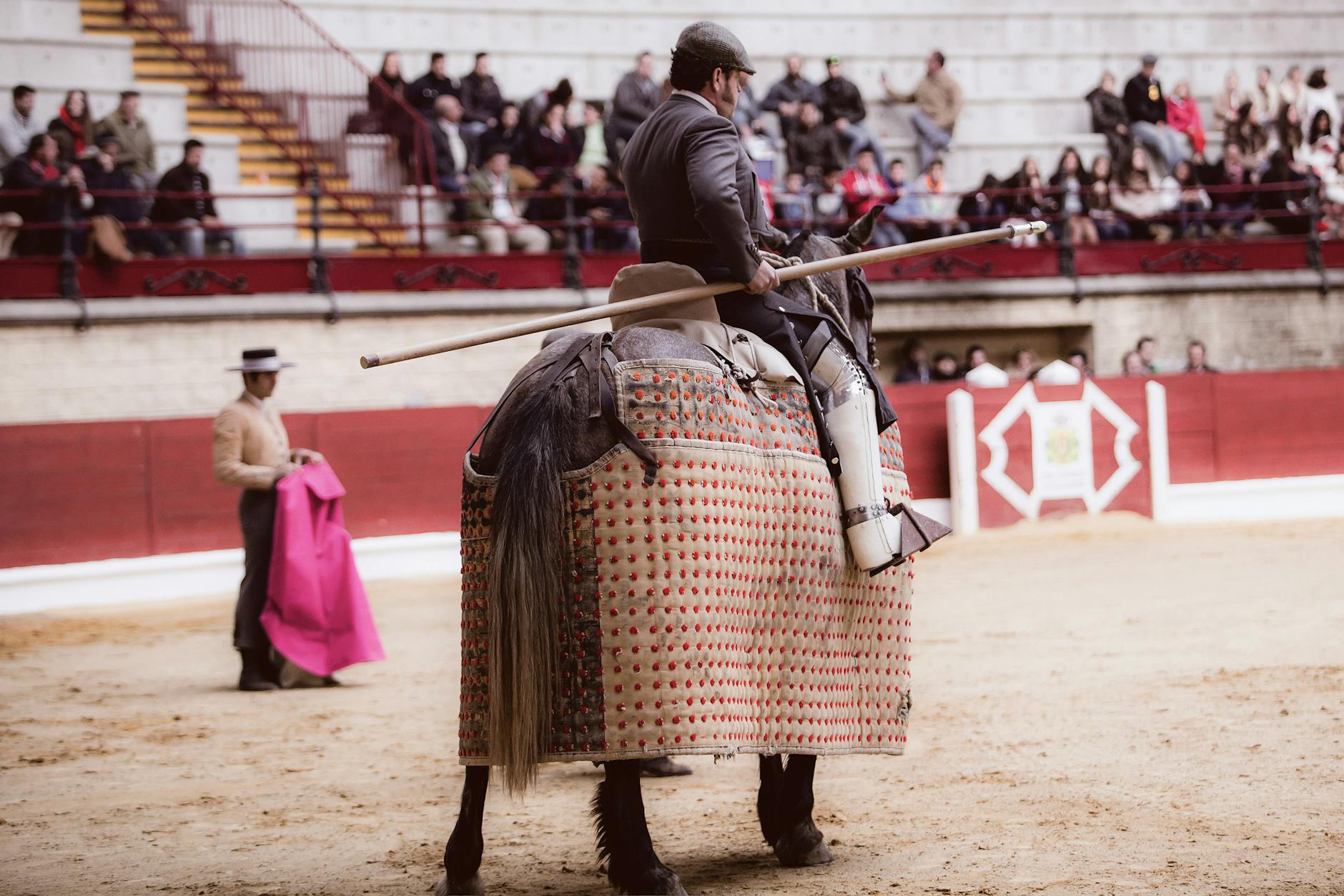 A picador on horseback with a lance prepares in a crowded bullring, showcasing traditional Spanish culture.