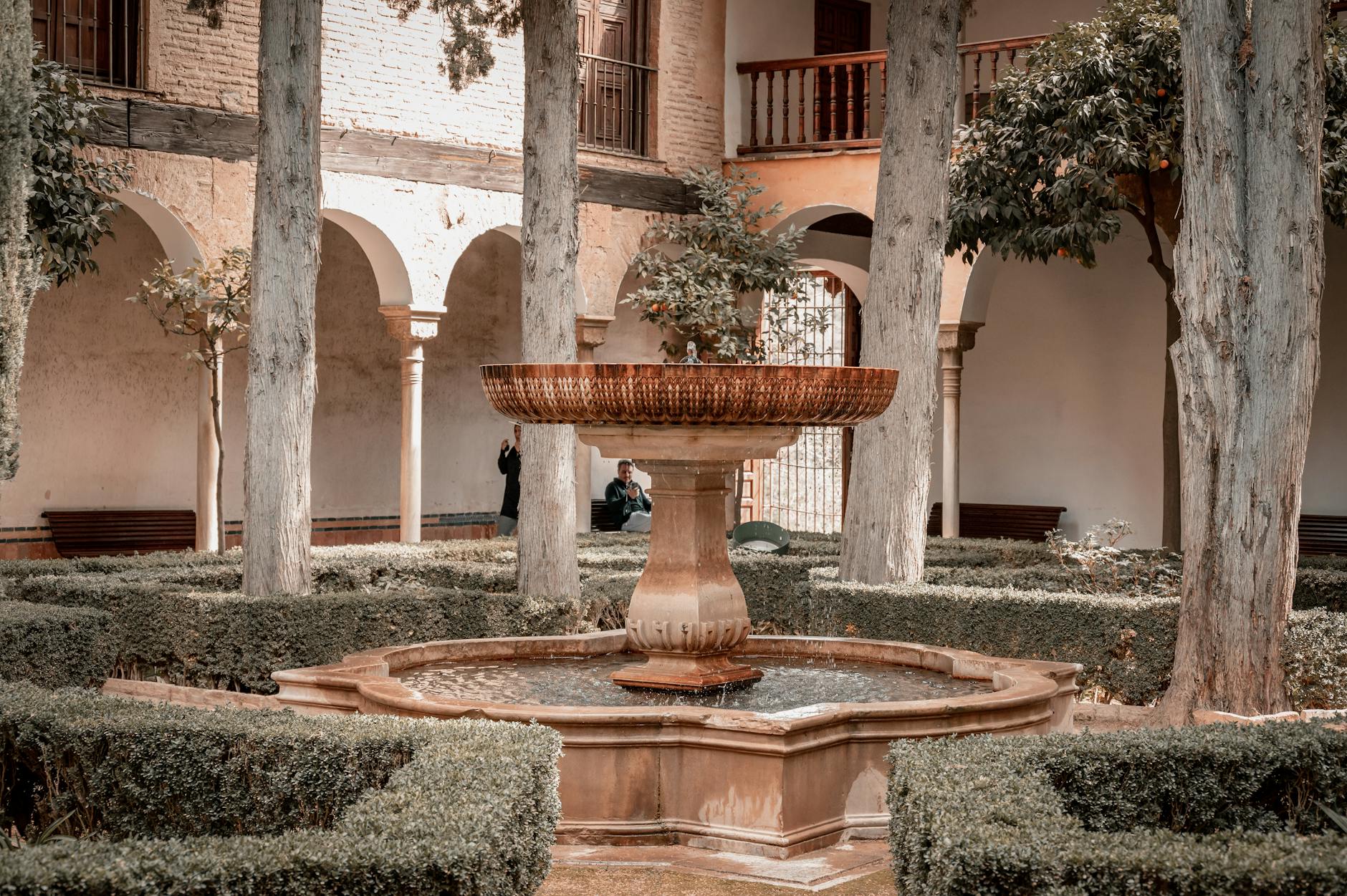 A serene courtyard in Granada featuring a central fountain surrounded by arches and greenery.
