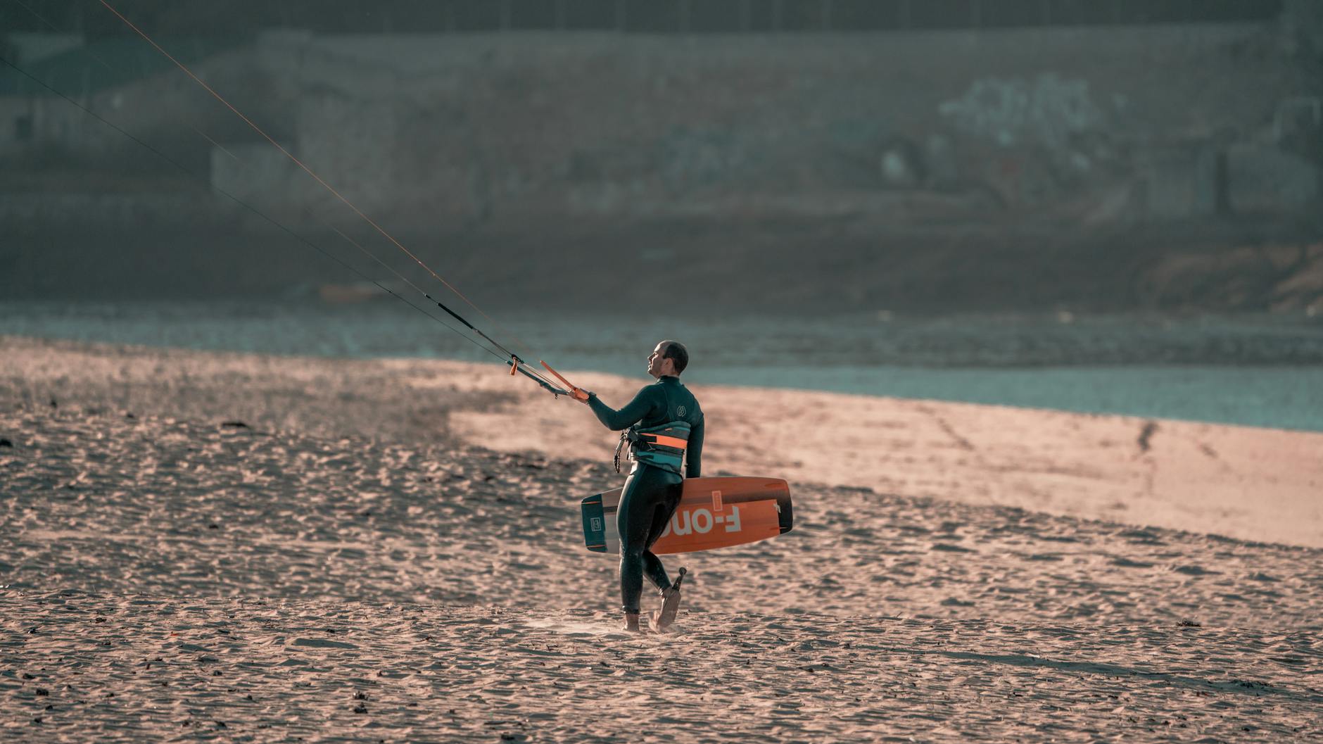 A kitesurfer carrying equipment on a sandy beach during dusk in Spain, capturing a serene moment.