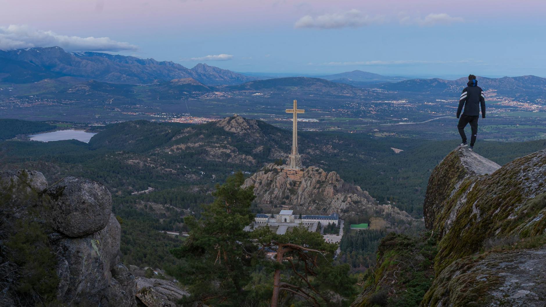 Hiker standing on a cliff overlooking the Valley of the Fallen in the Sierra de Guadarrama, Spain.