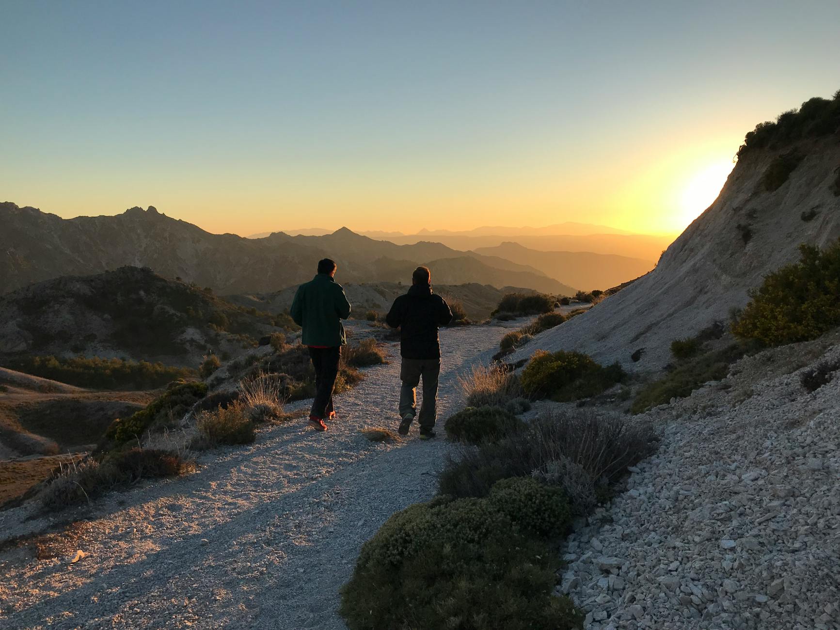 Two hikers walking on a path in Sierra Nevada, Spain at sunrise with a stunning mountain view.