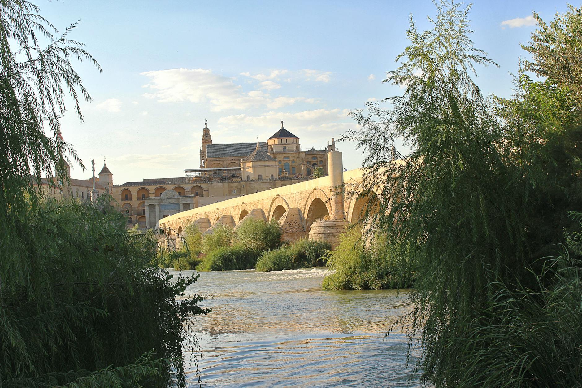 Capture of the historic Roman Bridge and Mezquita in Córdoba, Spain, surrounded by lush greenery and river reflections.