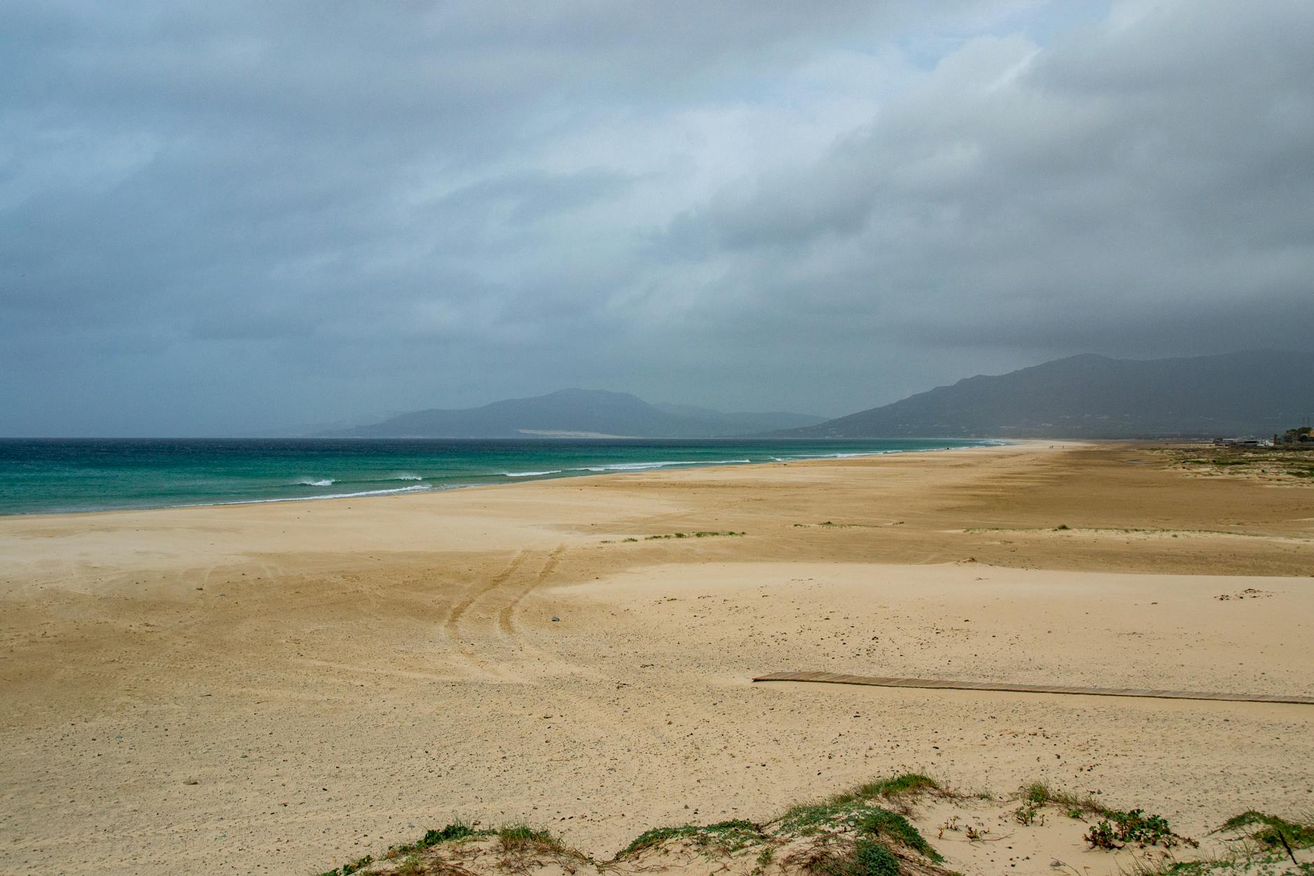 Calm and expansive sandy beach in Tarifa, Spain with cloudy sky and distant hills.