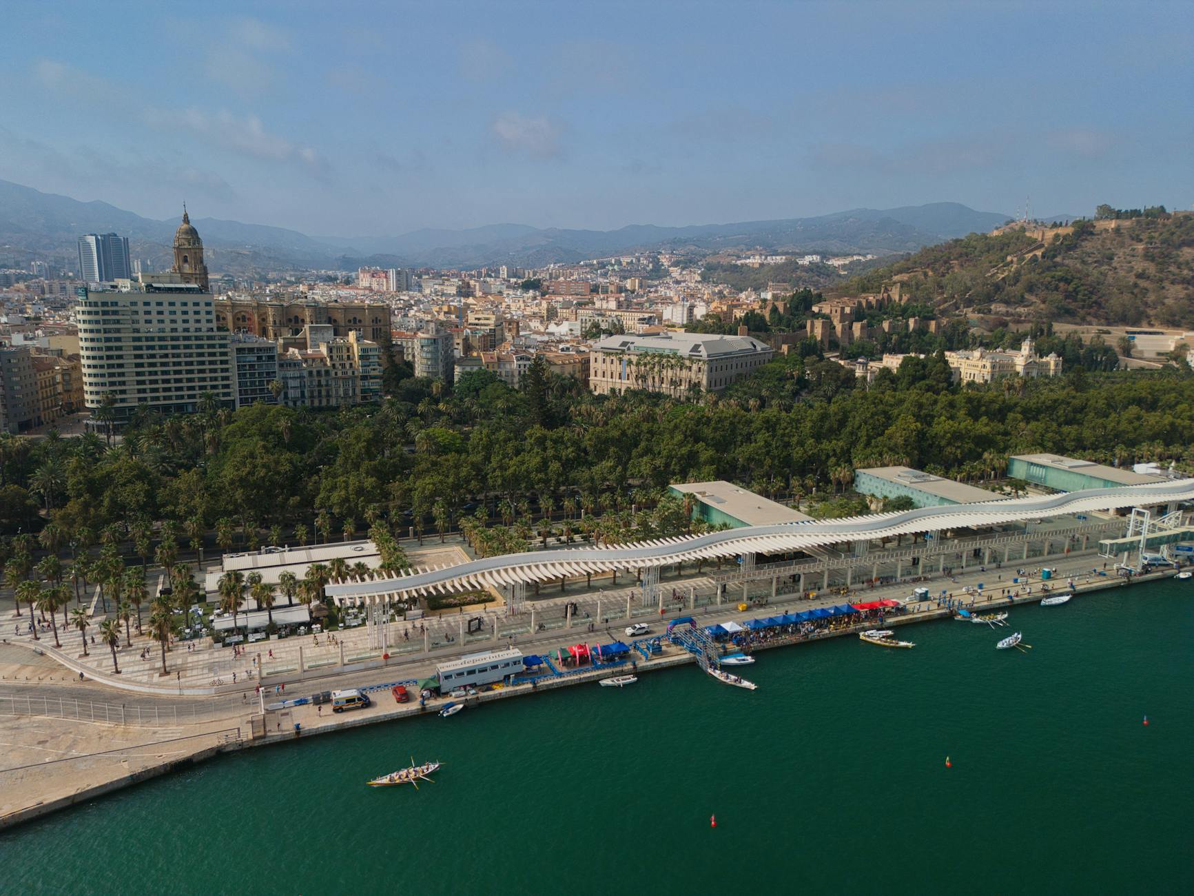 Explore the scenic Málaga harbor and cityscape with lush greenery and vibrant waterfront.