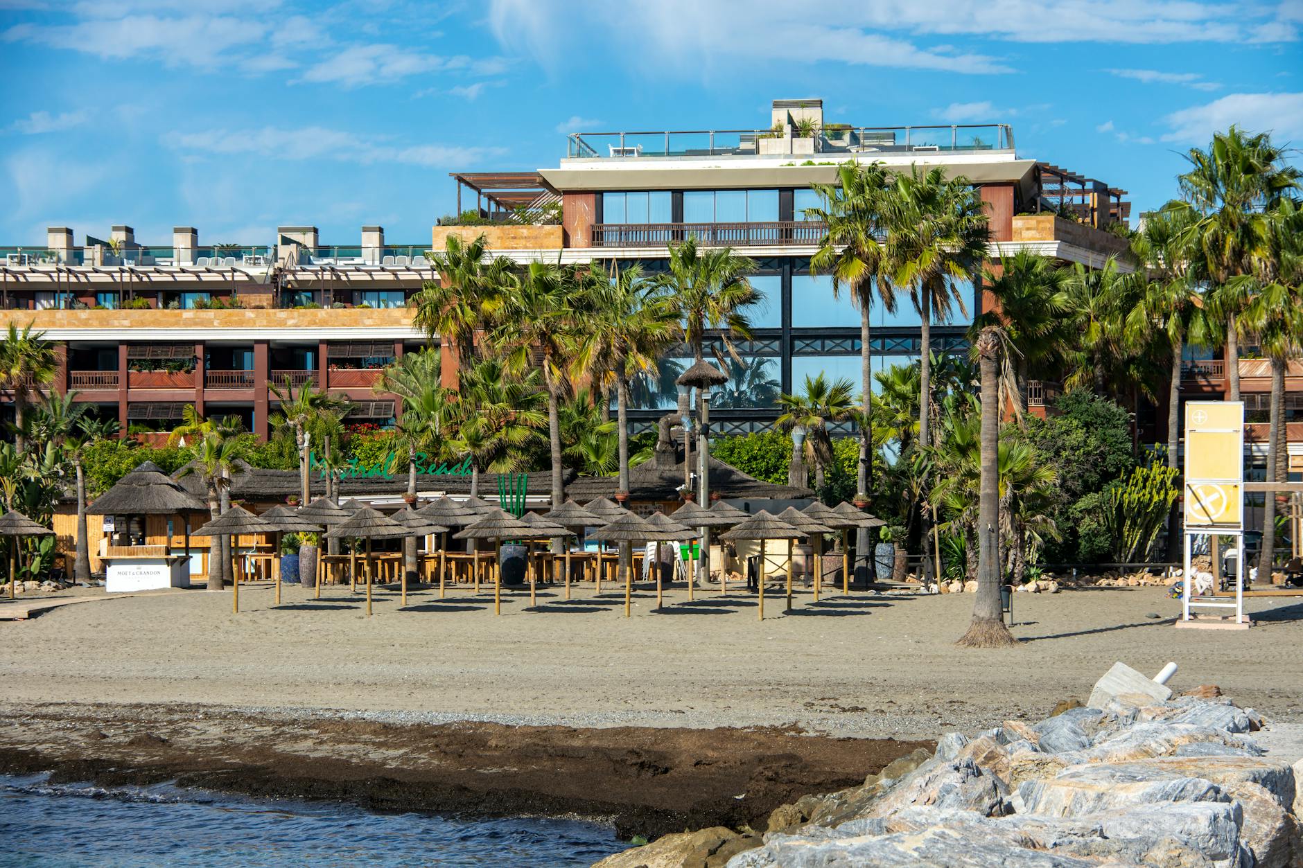 Scenic view of a beachfront building with palm trees and beach huts in Marbella, Spain.