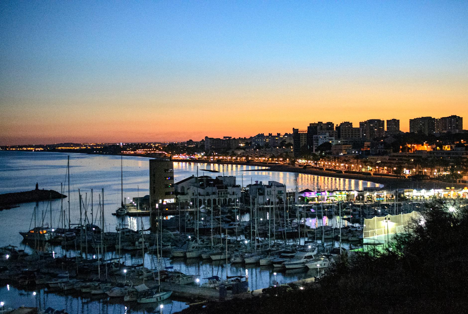 Scenic view of Aguadulce marina and city skyline at sunset, reflecting vibrant colors on the water.