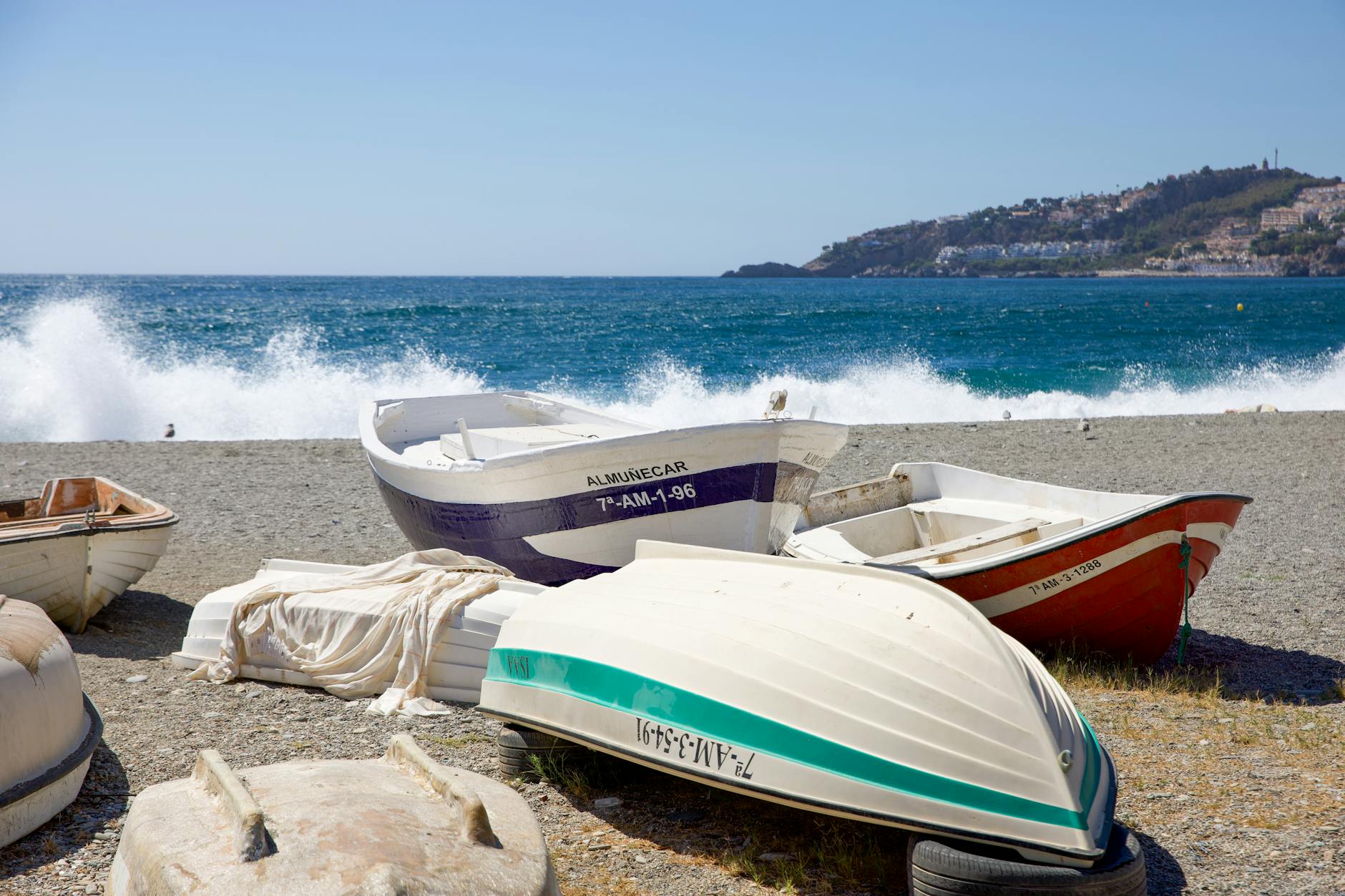 Colorful boats resting on Almuñécar beach with waves crashing in the background under a clear blue sky.