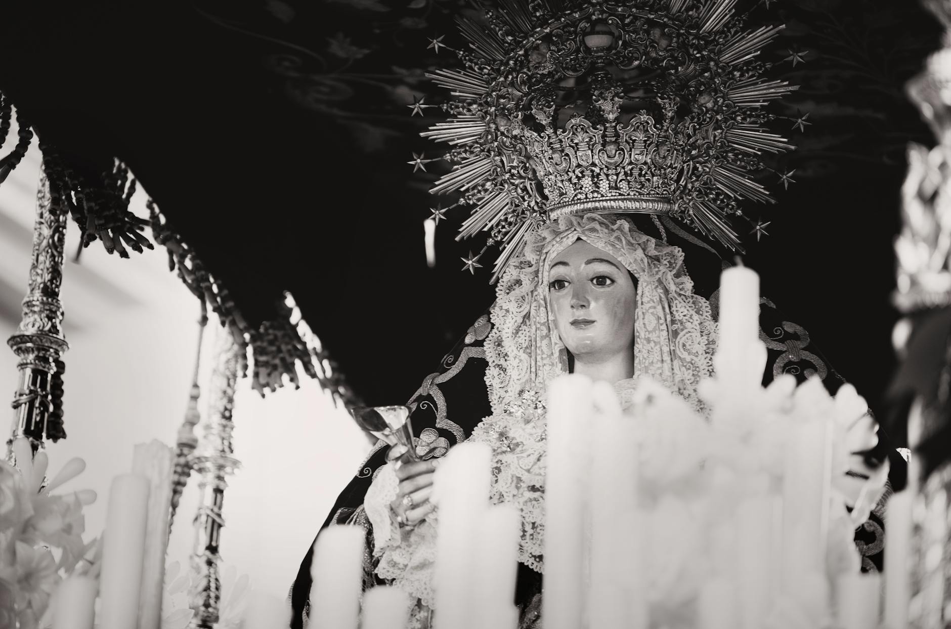 A serene black and white image of a religious statue surrounded by candles in Carmona, Spain.
